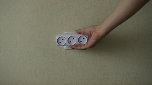 Mãos aproximadas de um homem irreconhecível inserindo uma camiseta branca de tomada elétrica ou um adaptador triplo em