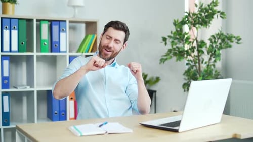 Happy and cheerful office worker dancing at work sitting at a computer desk. enjoy after successful
