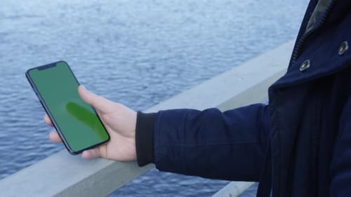 Tap and swipe on a cell phone while standing near water green screen