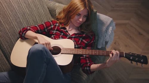 Woman Plays Acoustic Guitar on Couch Indoors
