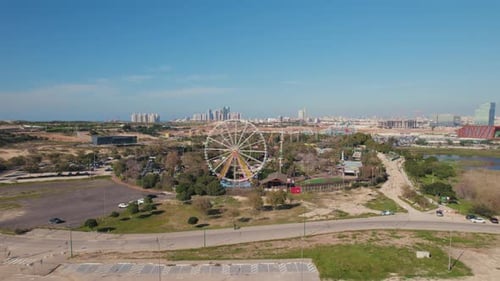 parallax shot from a distance of a Ferris wheel in a small theme park on a sunny day without clouds