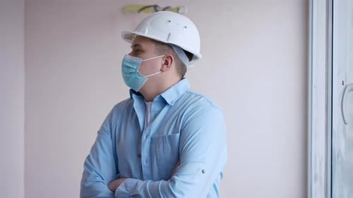 Professional Young Foreman in Covid19 Face Mask Crossing Hands Looking Around Standing in Building