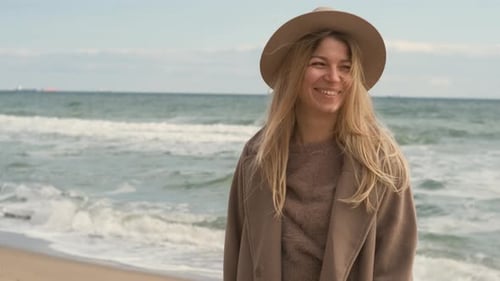Portrait of Romantic Blonde Woman Walking in Hat and Coat on the Beach in Autumn Sunny Day
