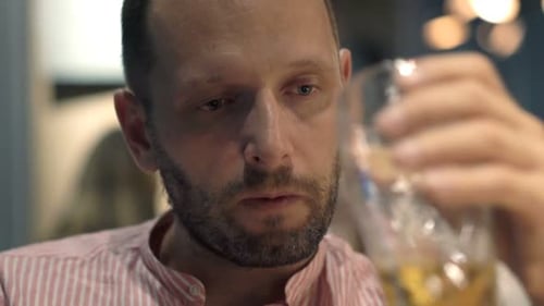 Sad man drinking beer alone in cafe at night contemplates his troubles