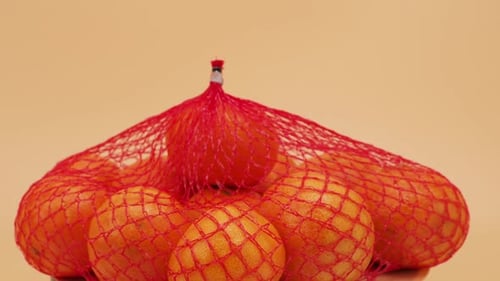 A group of tropical tangerine fruits in a mesh package rotate on an orange background.