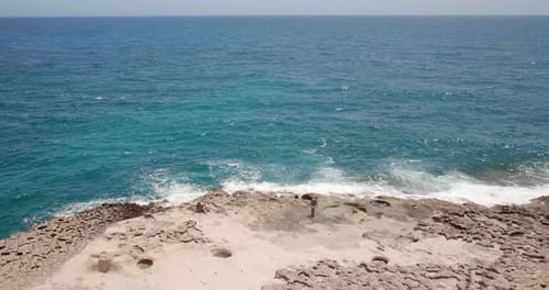Lonely man fetching water in bottle near ocean. Rocky seacoast with big waves. Mediterranean sea wit