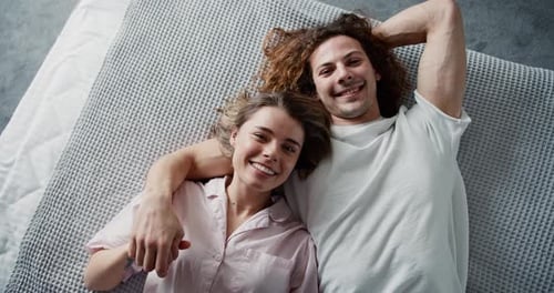 Süße Millenial-Liebhaber schauen auf ihrem Bett in die Kamera, Ansicht von oben