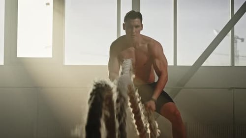 Engagierter motivierter kaukasischer männlicher Athlet trainiert hemdlos im Fitnessstudio mit Battle Ropes