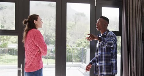Enojada pareja diversa discutiendo junto a la ventana de su casa, Cámara lenta