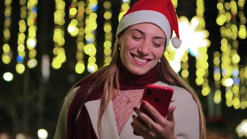 Smiling Woman with Phone and Santa Hat at Night