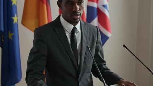 Man in Suit Speaking Behind Podium With Flags