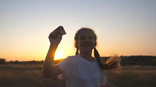 Happy Small Girl Running with Paper Airplane Through Grass Field