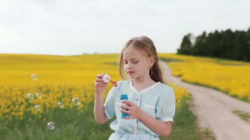 Cheerful Girl Blowing Soap Bubbles Among Yellow Field