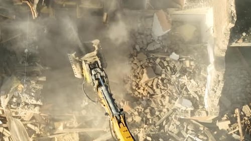 Images aériennes d'une excavatrice détruisant méthodiquement la structure d'un bâtiment pour la réduire en miettes