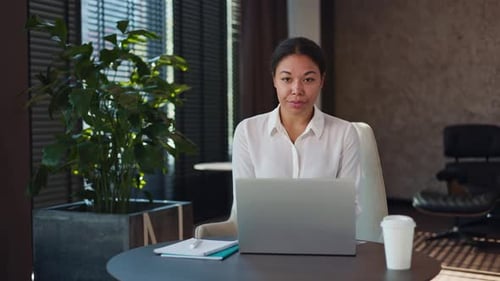 Pleasant Woman Smiling and Looking at Camera While Working on Laptop at Office