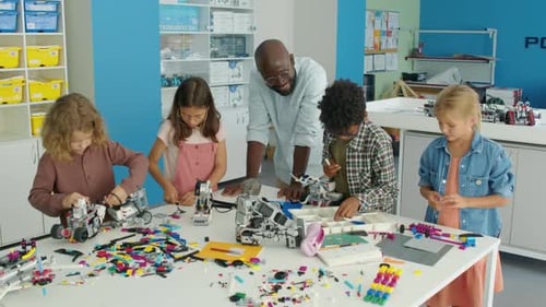 Profesor negro que observa a diversos niños construir robots de juguete en un club de pasatiempos