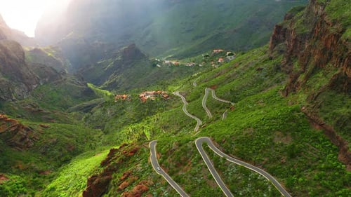 Winding road in mountains green landscape and glowing horizon during dawn with sun rays. Masca Gorge
