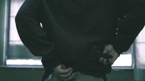 The male assassin put the gun in the rim of his pants, covered his hood, criminal man walking