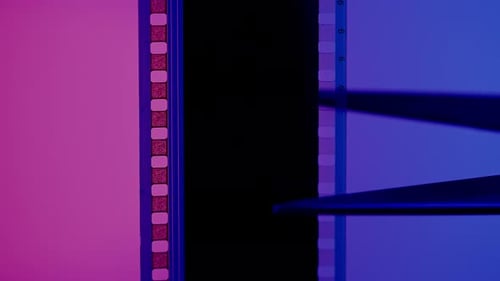 Las tijeras cortan una tira de película fotográfica sobre un fondo azul y rosa de cerca