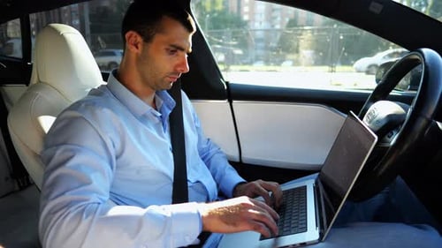 Handsome Entrepreneur Working on Notebook While Riding an Autonomous Self Driving Electric Car at