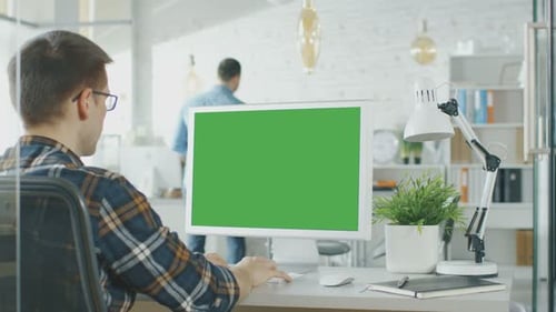 Close-up of a Man Sitting at His Desk with Green Screen PC on the Table. In Background Blurred and
