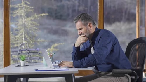 Man Works At Desk With Laptop Computer