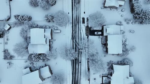 White snowy row of houses and street with tire marks in winter season. Aerial top down shot. Calm