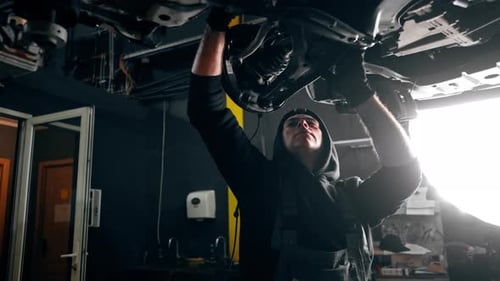 an Auto Mechanic at a Service Station Unscrews the Bolts Under the Body with a Wrench
