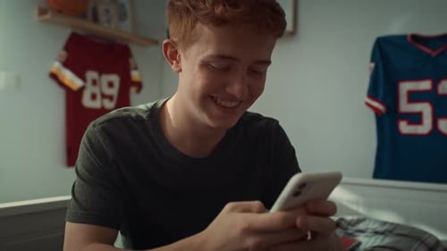 Close up of caucasian teenage boy browsing phone while sitting in his bedroom. Shot with RED helium