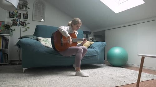 Woman playing guitar on a couch indoors