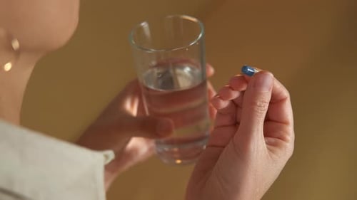 Woman Taking Pill with Water in Indoor Setting