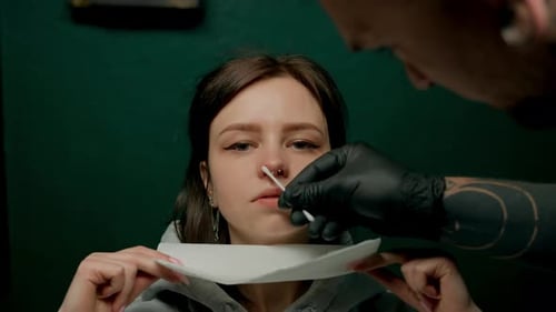 Interior de un estudio de piercings: el maestro de piercings hace un piercing para una niña, piercing para el tabique nasal