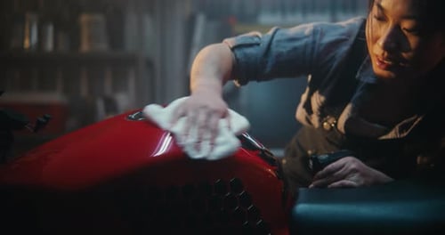 Young Woman Polishing a Red Motorcycle in a Dark Garage