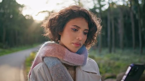 Attractive Girl Looking Cellphone at Sunny Autumn Forest in Casual Coat Closeup