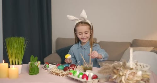 Little Girl Painting Easter Egg on a Table at Home