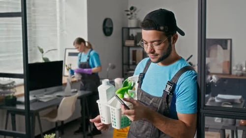 Specialist Checking Smartphone Holding Cleaning Supplies at Office Workspace