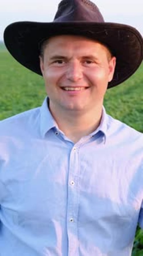 A Cheerful Farmer Wearing a Stylish Hat Proudly Stands in a Lush Green Field