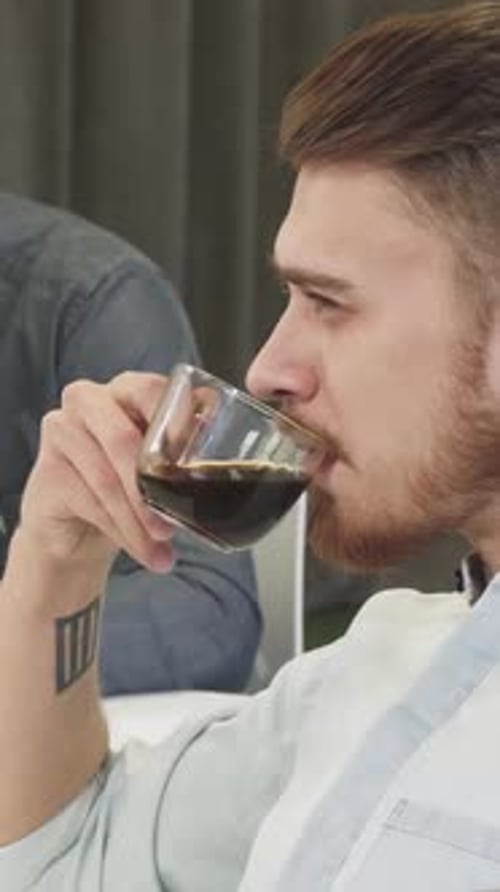 Two Men Talking, One Drinking Dark Beverage