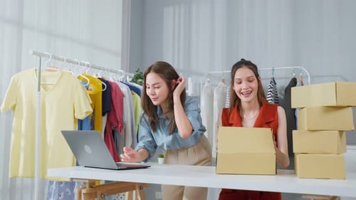 Asian two beautiful woman packing clothes order into box for customer.