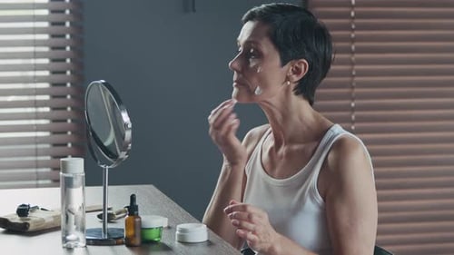 Woman Applying Face Cream in the Mirror Indoors