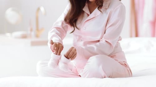 Pregnant Woman Holding Baby Booties on Bed in Bedroom