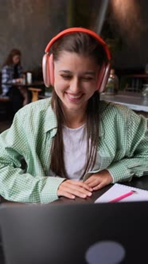Smiling Woman Uses Laptop at Table with Headphones