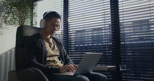 Man Works on Laptop Wearing Headphones Indoors