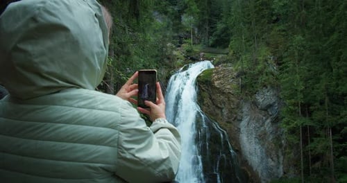 Woman tourist takes photos on phone of Golling waterfall in Austria.