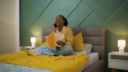 Young African American woman sitting in bed in the bedroom working using laptop.