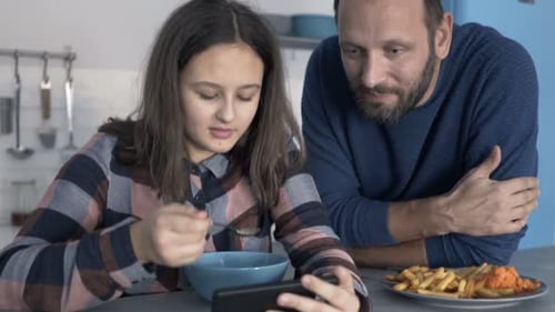 Teenage Girl and Man Watching Phone While Eating