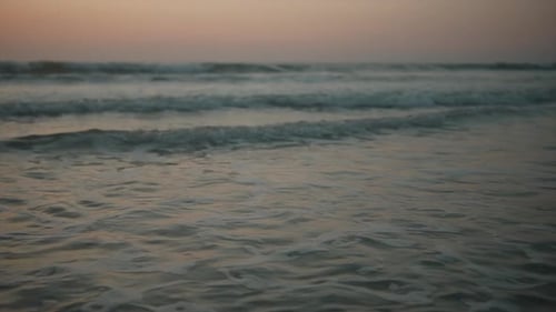 Kleine schäumende Wellen rollen ruhig über das Ufer und spülen im Morgengrauen über den Sand