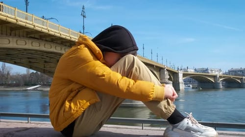 Um adolescente em desespero se senta à beira da ponte