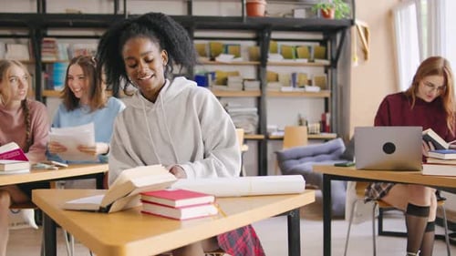An African American Female Student Sits in Class Surrounded By Books and Papers Taking Detailed