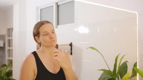 Woman Using Pink Jade Roller on Face in Bathroom, close view, Facial Massage Concept